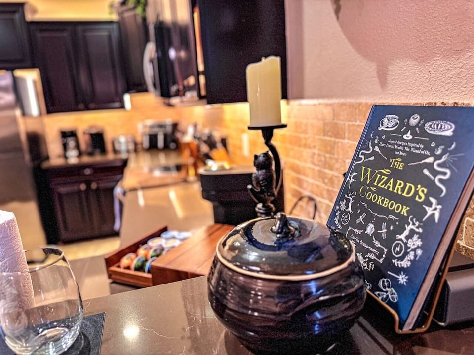 A cast-iron owl guards the counter beside The Wizard’s Cookbook. Behind curved glass, a 1900s Ferguson Brothers apothecary cabinet holds potion jars and mandrake root. Open a cabinet — the lights come on. Something stirs.