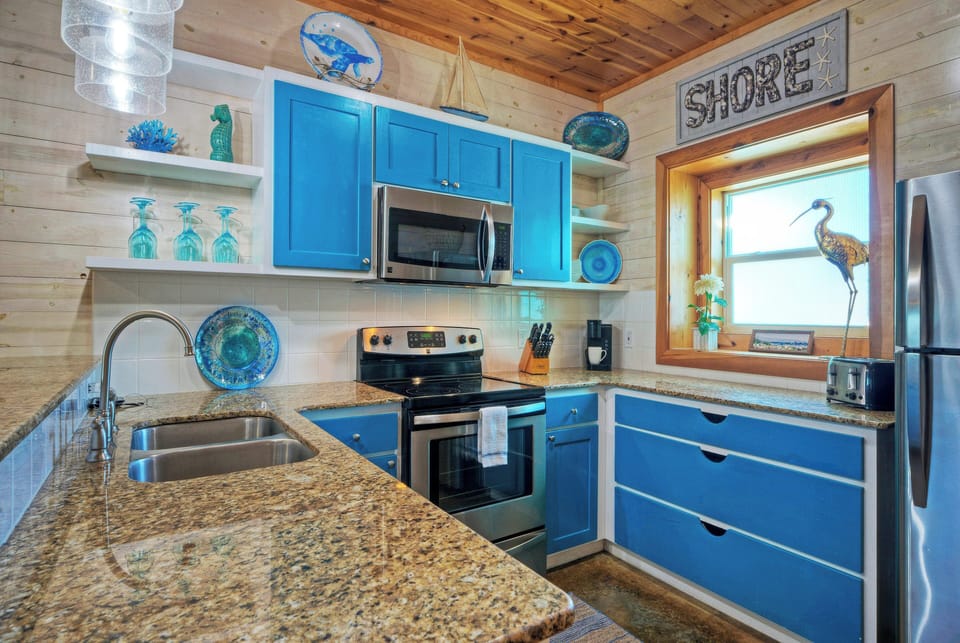 Bright, beachy kitchen with coastal-blue accents, stainless appliances, and easy flow into the dining and living spaces.