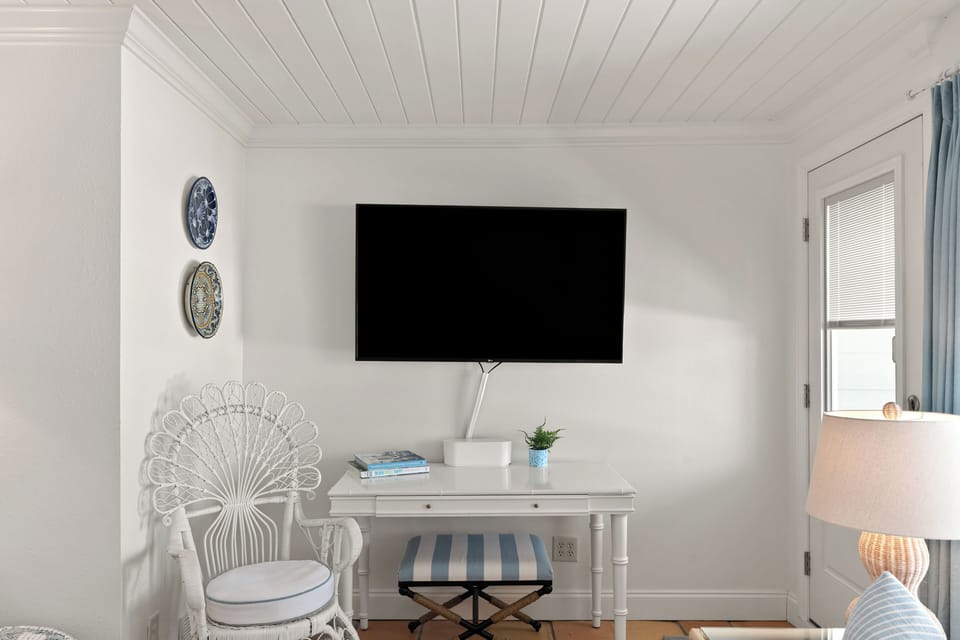 Dedicated bedroom desk or vanity workspace featuring a wall-mounted TV and a matching white wicker chair.