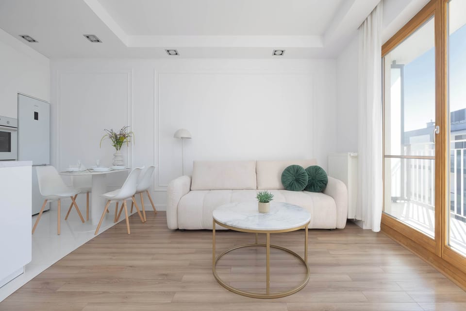 An open-plan living area combining a sofa lounge and a kitchen in a sleek, modern layout. A sliding glass door brings in plenty of daylight and connects the interior to the outside.