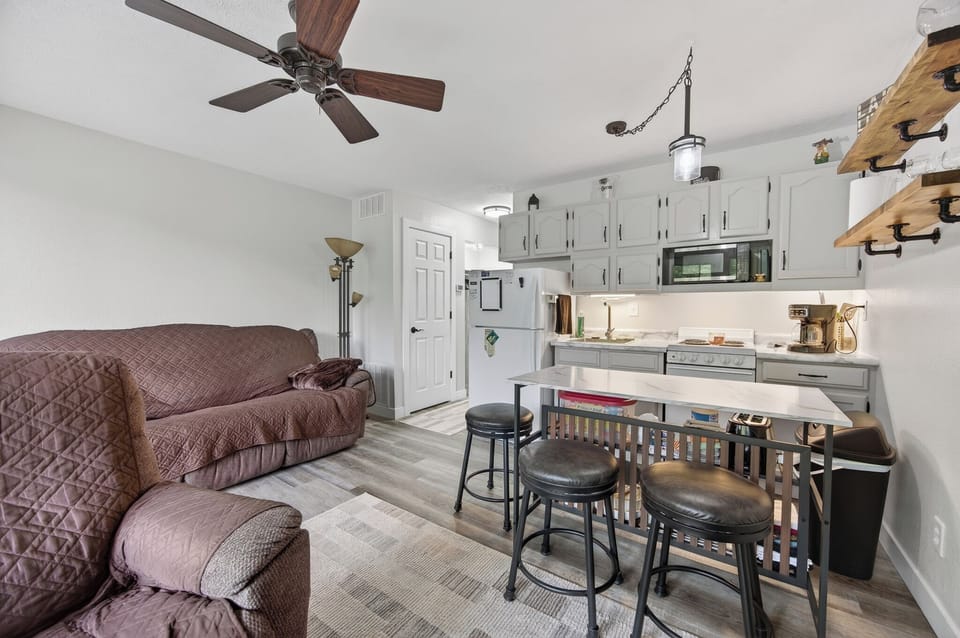 Your cozy retreat features a full kitchen with modern appliances, a comfortable living area with ceiling fan, and a breakfast bar perfect for morning coffee or casual meals together.