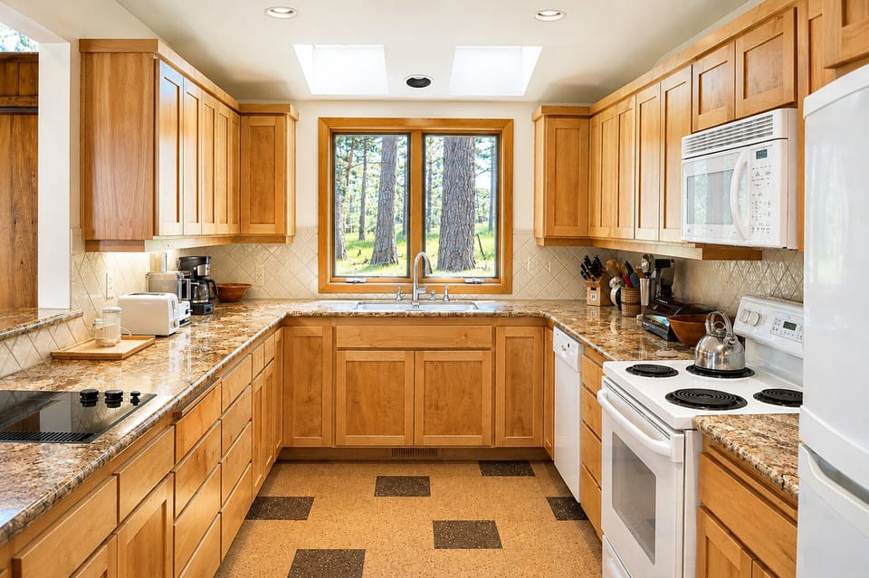 Your fully equipped kitchen features granite countertops, warm oak cabinetry, and forest views through the window—perfect for preparing meals during your stay.
