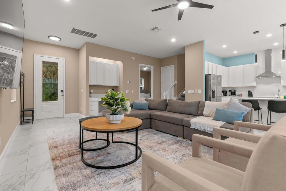 Open-concept living area with a sectional sofa and modern kitchen featuring white cabinetry and stainless steel appliances.