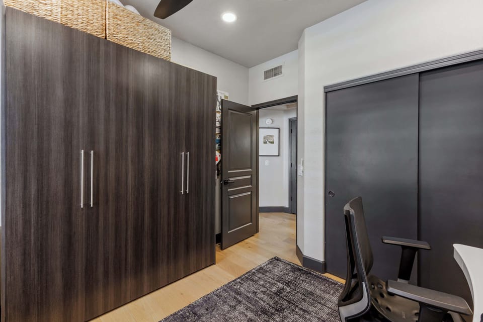 This flexible second bedroom doubles as a dedicated office, featuring a Queen Murphy bed, sleek workspace, ergonomic chair, and a closet for convenient storage.