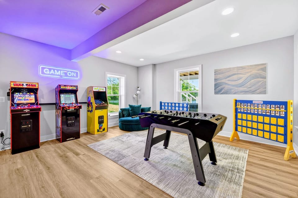 Game Room - Trio of arcade cabinets, NBA Jam, Mortal Kombat, and Pac-Man, line the wall beneath the glowing blue GAME ON sign by a sunny window.