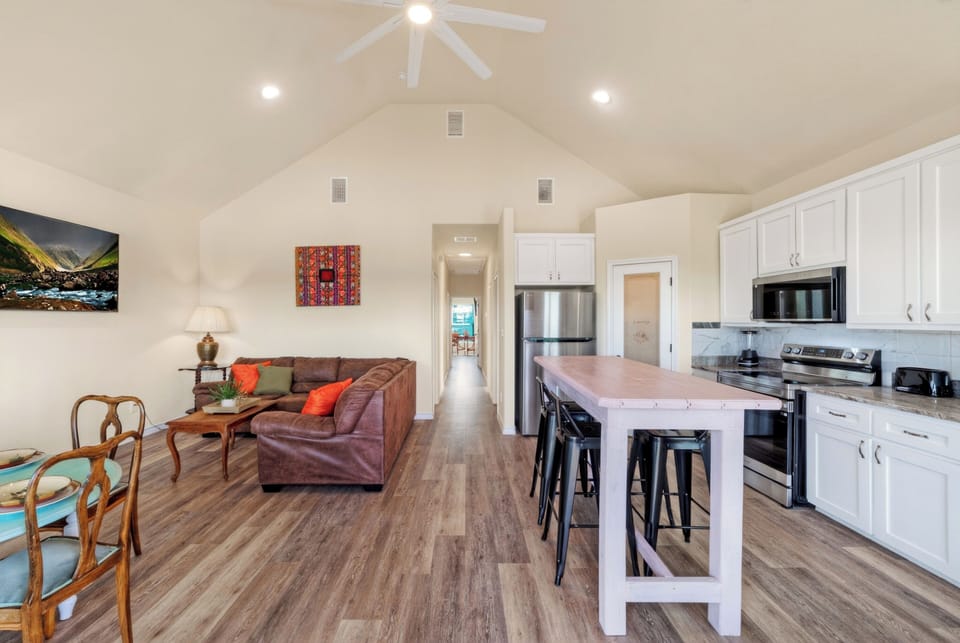 Open-concept living and kitchen area with vaulted ceilings, island seating, and relaxed coastal style.