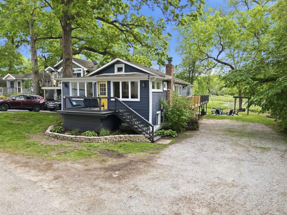 Street-level curb appeal — blue cottage with yellow door, fire pit visible in back