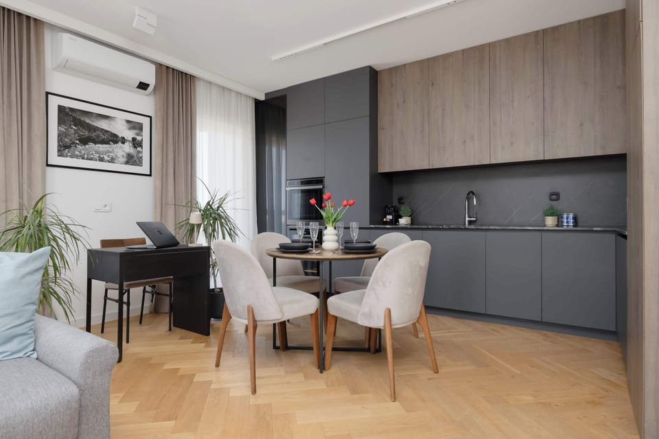 A dining area connected to a modern kitchenette with dark cabinets. The room is bright and spacious.