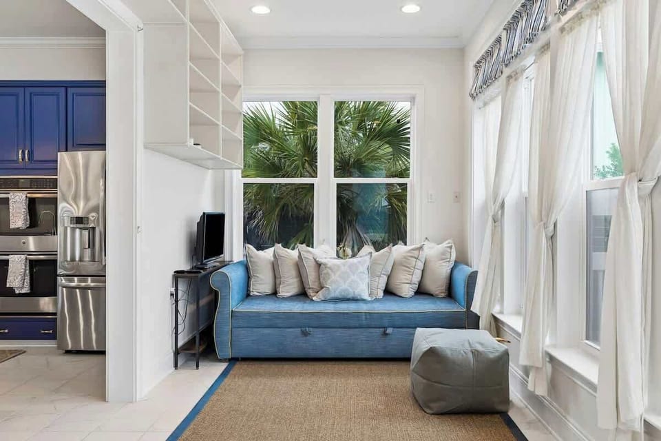 Cozy Sunroom Lounge

A bright, sunlit nook featuring a comfortable blue daybed stacked with plush pillows, a natural jute rug, and a modern gray ottoman. Framed by large windows overlooking tropical greenery, it makes the perfect reading retreat.