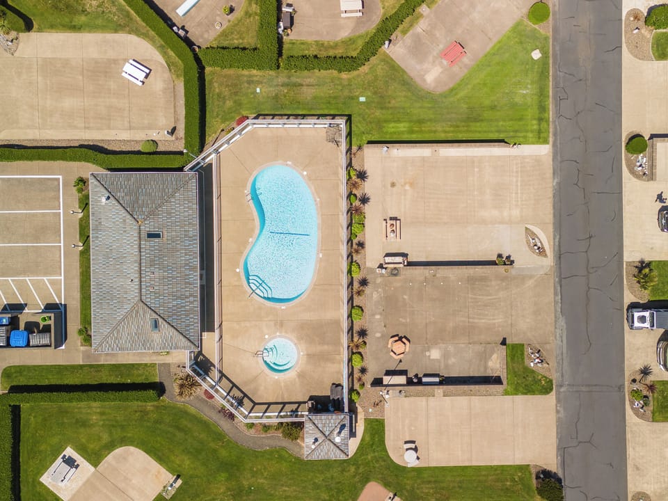 Aerial view of the property showcasing a kidney-shaped swimming pool, hot tub, tennis court, and well-manicured grounds in a residential neighborhood.