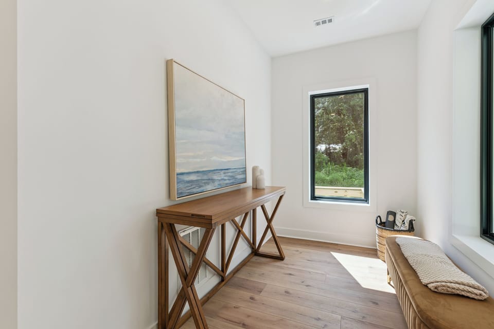 Step into your serene entryway, where natural light streams through the window and warm wood floors create a welcoming atmosphere for your coastal getaway.