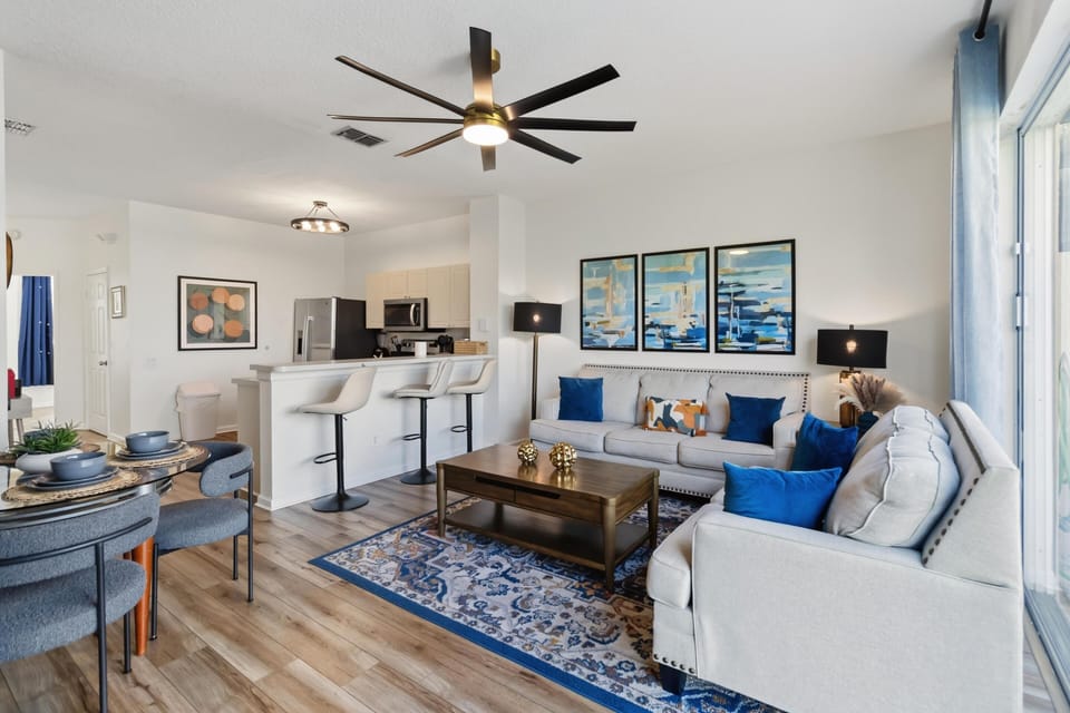 Living room with light gray sofas, blue accent pillows, patterned rug, and large sliding glass doors.
