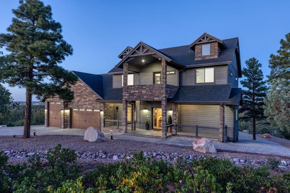 As the sun sets, warm architectural lighting transforms the home into a welcoming mountain sanctuary nestled among the pines.