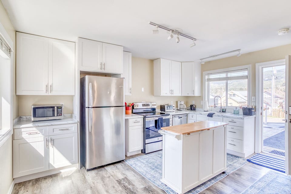 Cook together in your bright, fully-equipped kitchen featuring modern appliances, ample counter space, and abundant natural light streaming through large windows.
