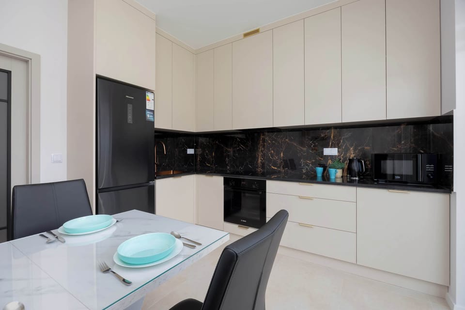 A modern kitchen with white cabinets, black finishes, and a dining table. The space is bright and elegantly designed.