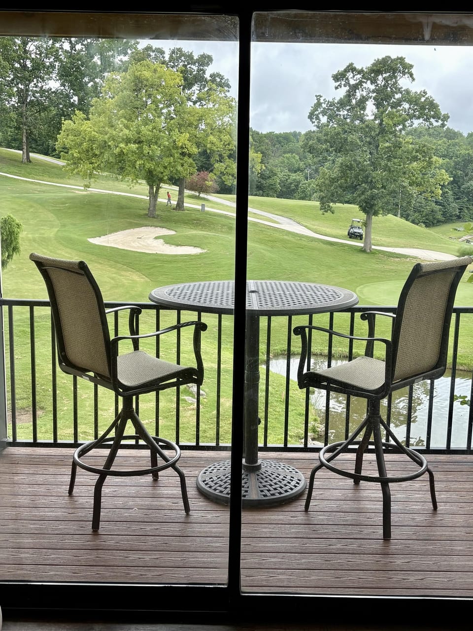 Balcony with two swivel bar chairs and a round metal table overlooking a golf course and pond.