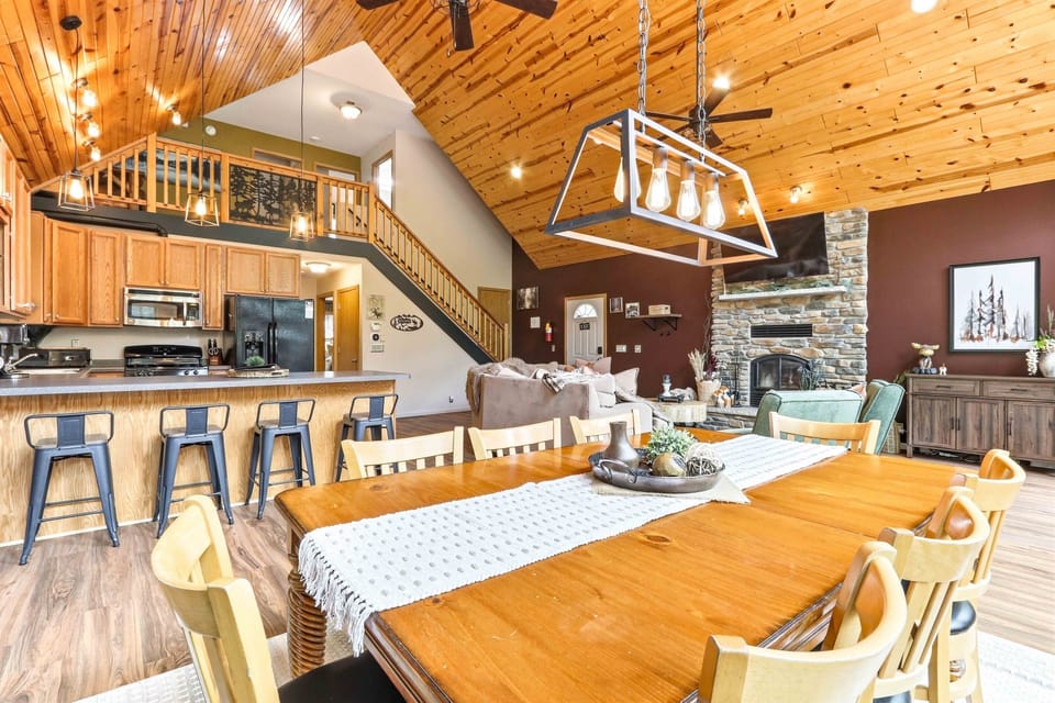 Beautiful cabin-inspired gathering space featuring a large dining area, breakfast bar seating, and a cozy great room with a stone fireplace.