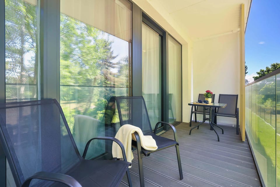 A sunny balcony overlooking the green surroundings, furnished with two comfortable, dark armchairs. Glass panels have been installed on the railing to provide a great view.