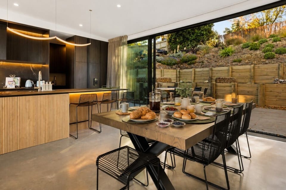 Gather around your spacious dining table where morning croissants and evening wine taste even better with hillside garden views through floor-to-ceiling windows”