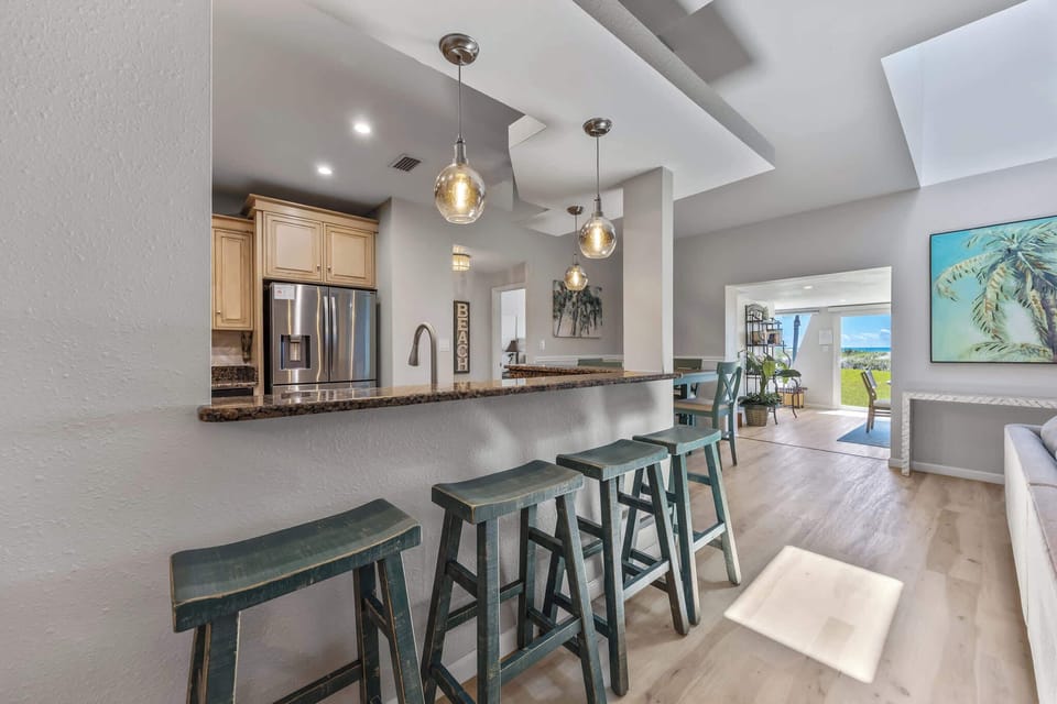 Modern kitchen bar with pendant lighting and seating that opens to a bright living area with ocean views.