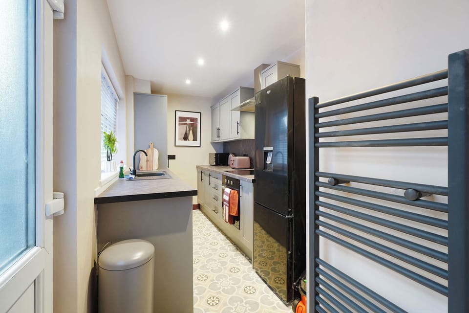 Enjoy a well-equipped kitchen featuring bright worktop space, a fridge freezer, and a heated towel rail nearby. The practical arrangement offers guests a convenient setting for cooking, preparing meals, and daily routines.
