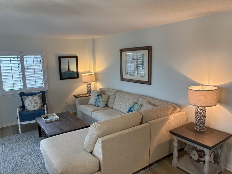 Living room with light beige sectional, navy accent chair, wooden coffee table, and table lamps casting warm light.