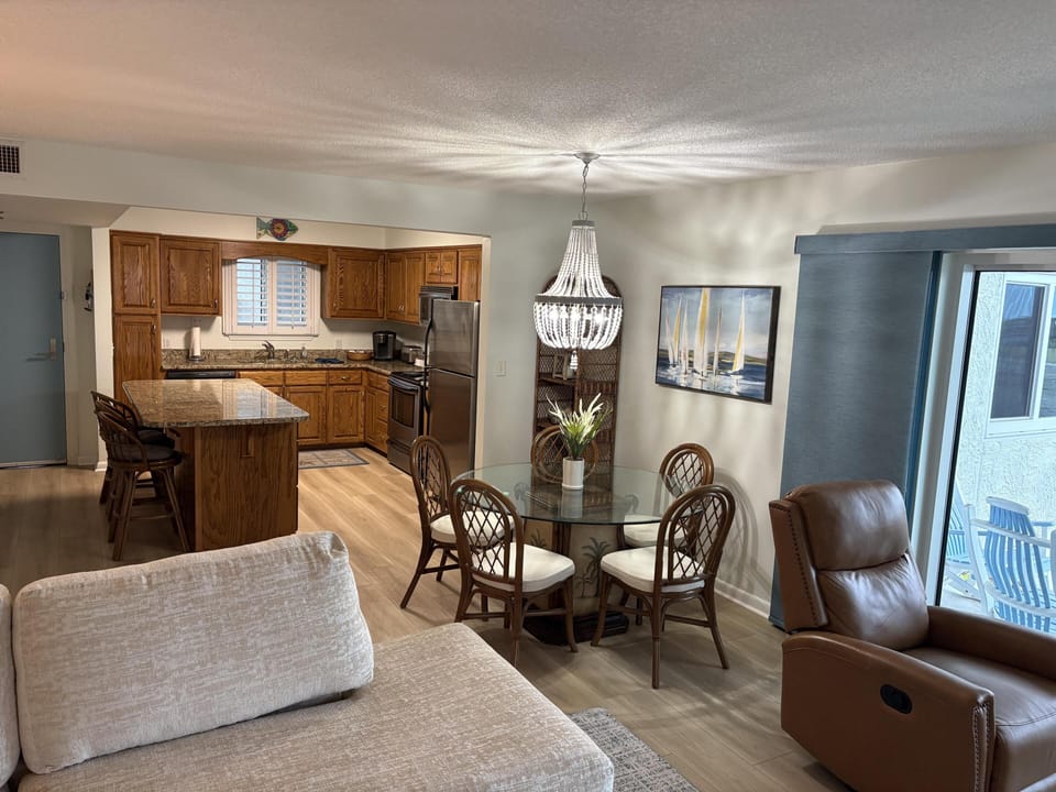 Open-concept kitchen and dining area with oak cabinets, granite island, glass table, and leather recliner.