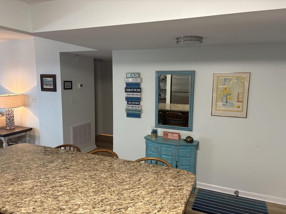 Granite countertop island overlooks a blue distressed cabinet with matching mirror and coastal wall art.
