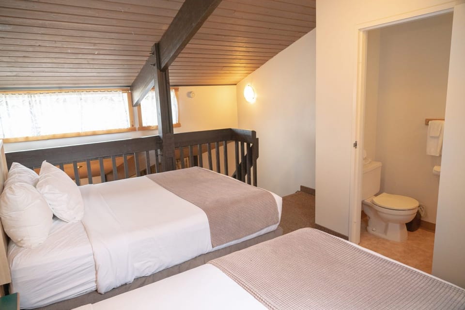 Loft sleeping area under wooden beam ceilings with two beds and a bathroom door to the right