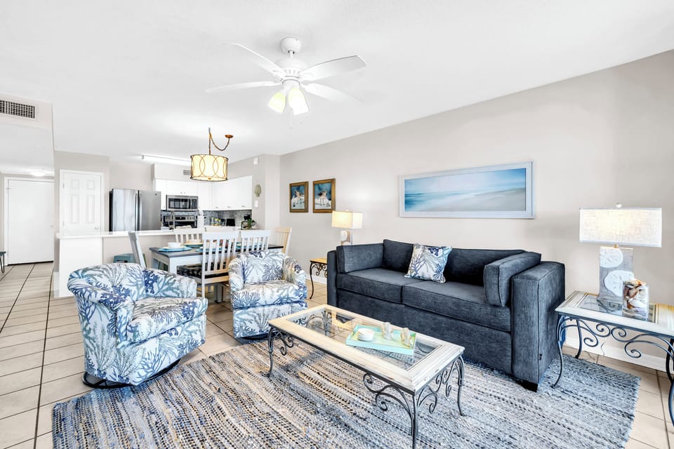 Bright, open living space where you can unwind on coastal-themed seating, gather around the dining table, and enjoy a breeze from the ceiling fan. The kitchen is just steps away.
