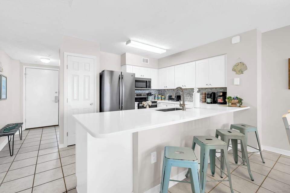 Whip up your favorite meals in this bright, modern kitchen with sleek white counters, stainless appliances, and a spacious island perfect for morning coffee.