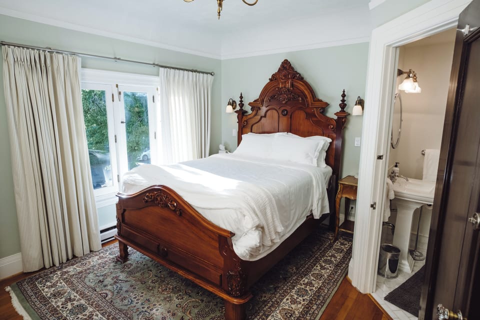 Elegant bedroom with carved wood bed, natural light, and en suite bath
