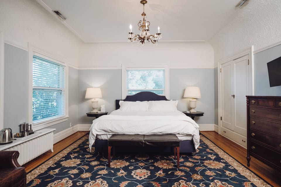 Elegant king bedroom with chandelier, hardwood floors, and natural light