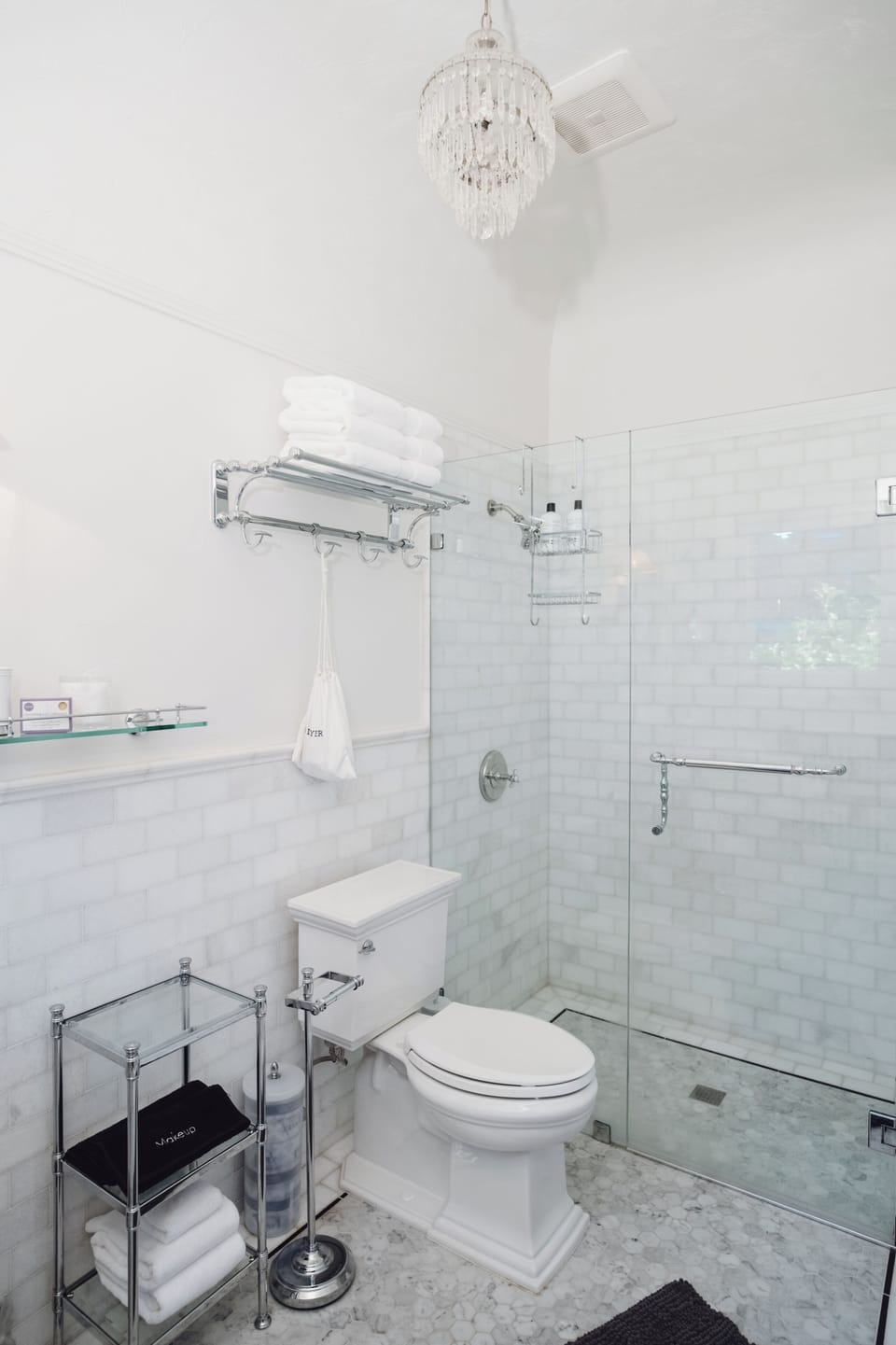 Elegant white-tiled bathroom with glass shower and chandelier charm