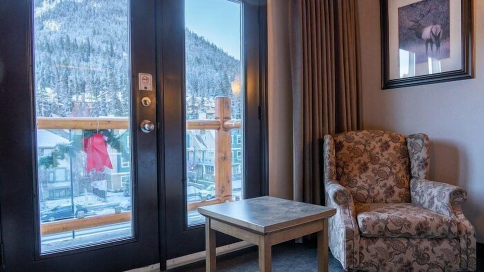 Snow-dusted mountains and evergreens framed through the balcony doors on a winter afternoon