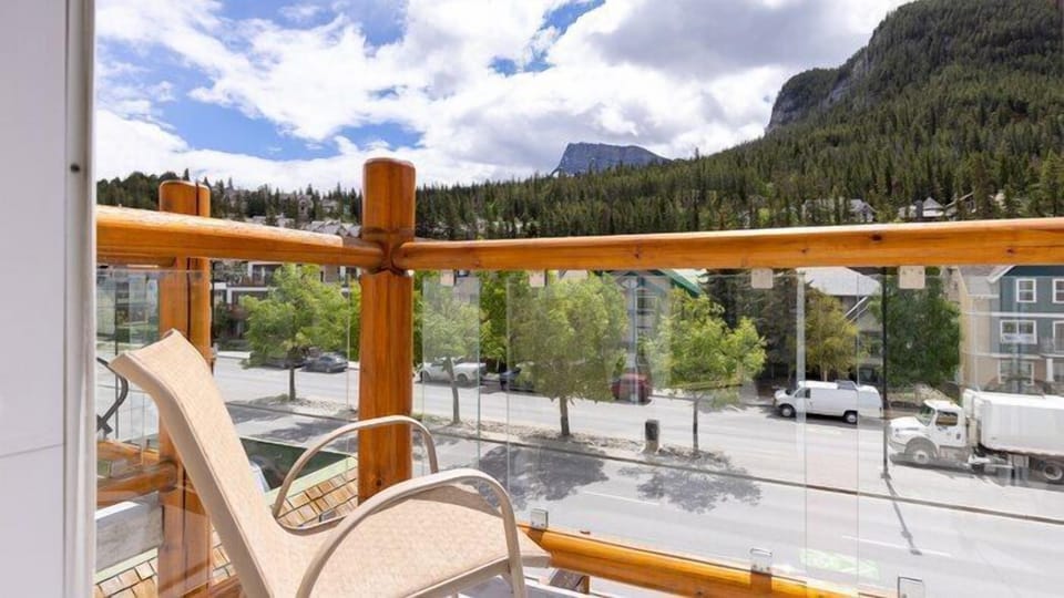 Balcony chair overlooking tree-lined street with mountain backdrop