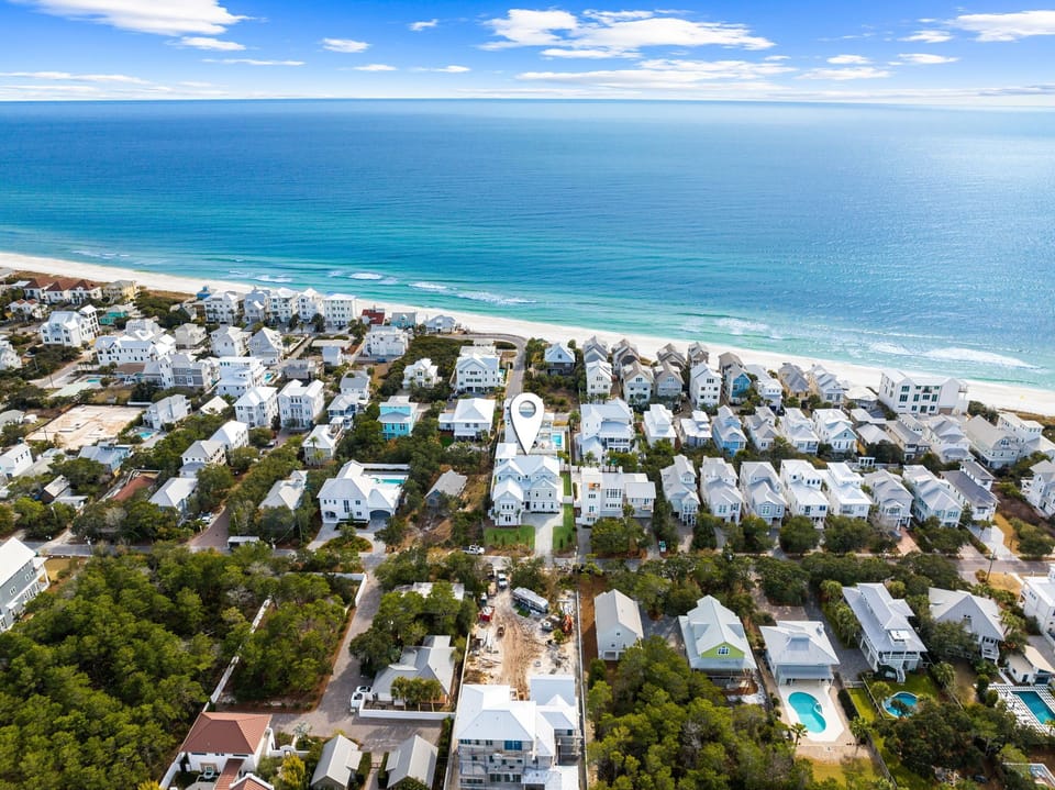 Aerial view of a charming beachfront community along Florida's Gulf Coast, with white sandy shores meeting turquoise waters and coastal homes nestled among lush greenery.