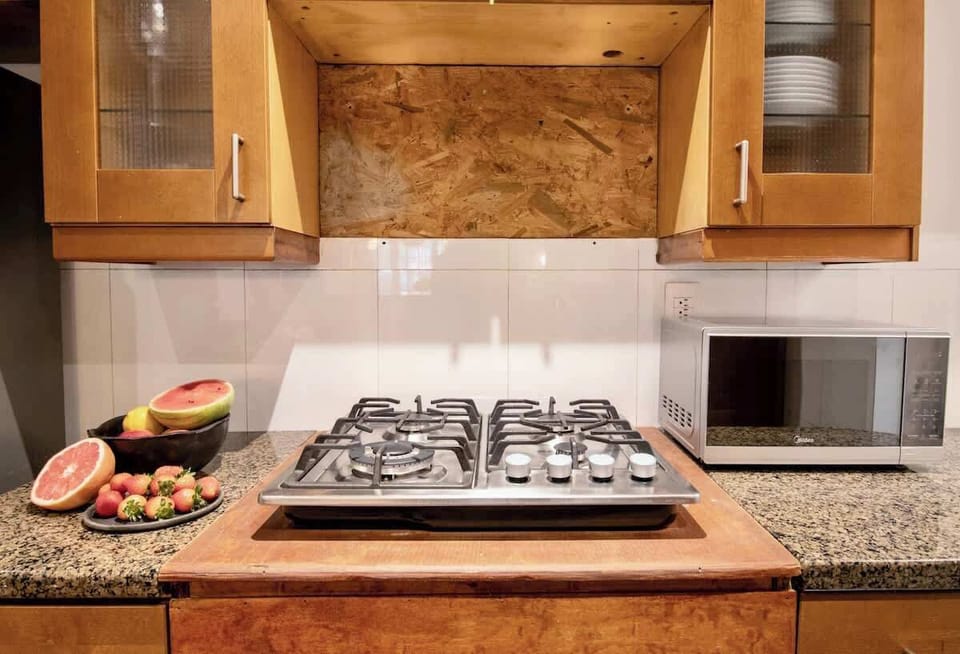 A practical yet inviting cooking space, where warm wood cabinetry meets stone countertops and modern appliances. Fresh ingredients within reach and clean lines throughout make everyday cooking feel simple, comfortable, and quietly enjoyable.