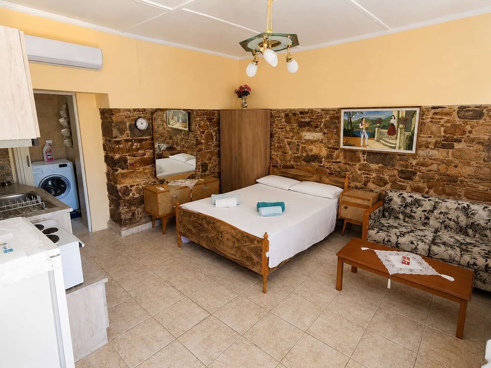 The studio features a comfortable double bed, stone-accented walls, warm décor, and a cozy atmosphere