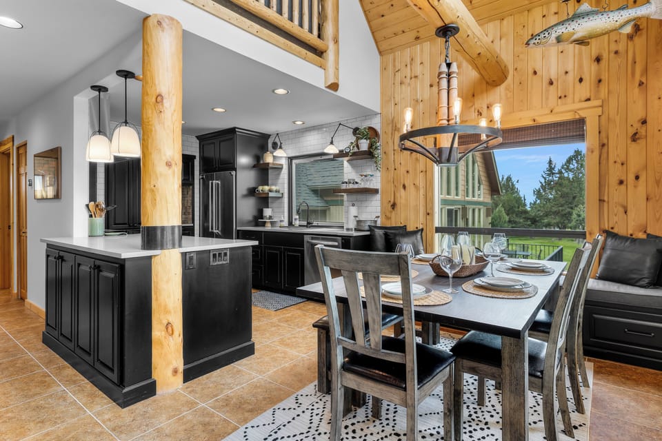 Gather around the rustic dining table where meals become memories, surrounded by warm wood beams and a sleek kitchen. Large windows frame views of lush greenery.