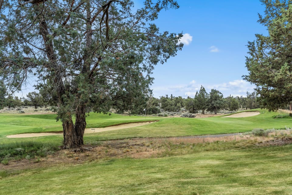 A pristine golf course winds through high-desert terrain, framed by native juniper trees and natural sagebrush. Sand bunkers and manicured fairways offer a scenic backdrop to the surrounding area.