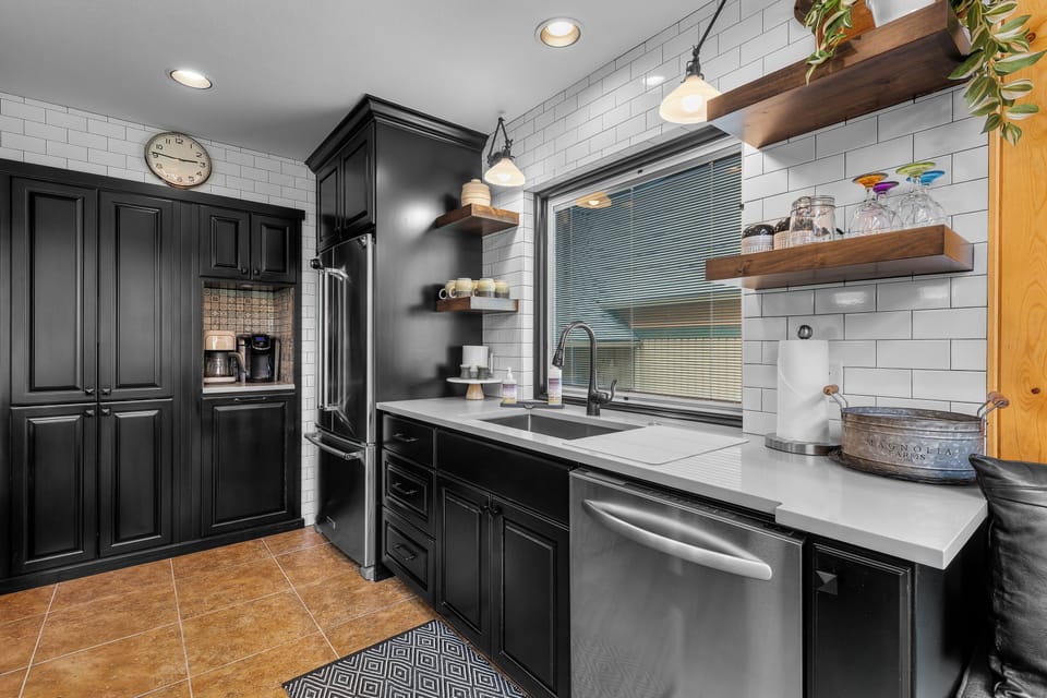 Step into your stylish kitchen, where sleek black cabinetry meets bright white subway tile. Rustic wooden shelves and modern stainless appliances make cooking a joy.