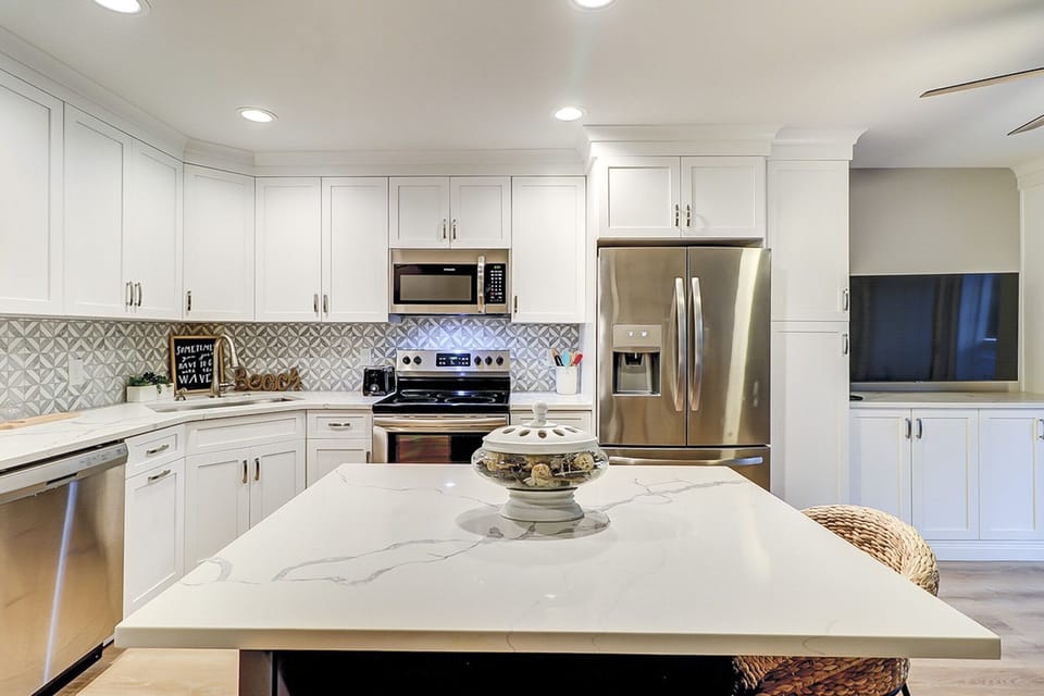 Veined marble counters and geometric tiles create a bright, contemporary chef's kitchen. Gleaming stainless steel appliances pair with snowy cabinetry to offer a fresh, airy space perfect for brewing morning coffee or preparing a shared feast.