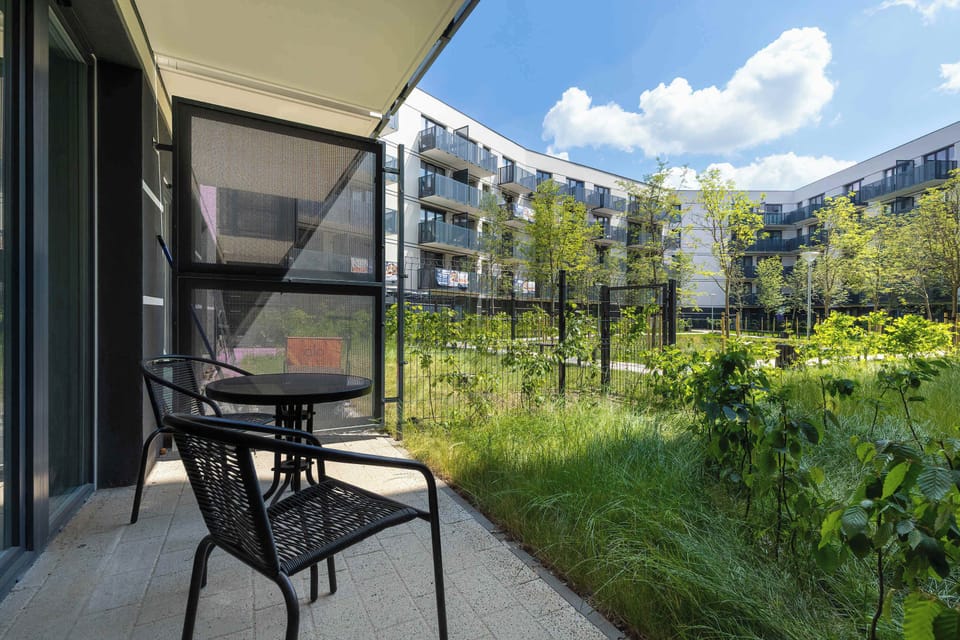 A green courtyard-style garden surrounded by modern apartment buildings. It offers a peaceful outdoor space with greenery and a pleasant view for relaxation.