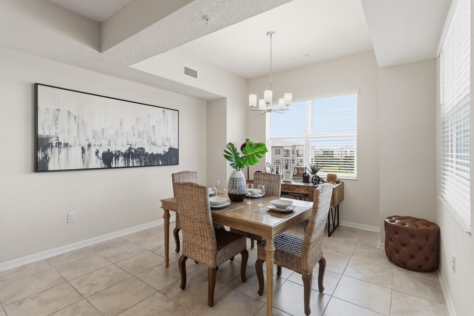 Natural light fills the dining area with a wooden table, woven chairs, and a monochrome cityscape painting.