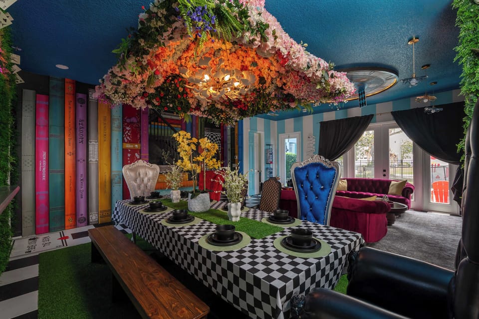 Dining area with a checkered tablecloth, floral ceiling installation, and colorful book-themed wall.