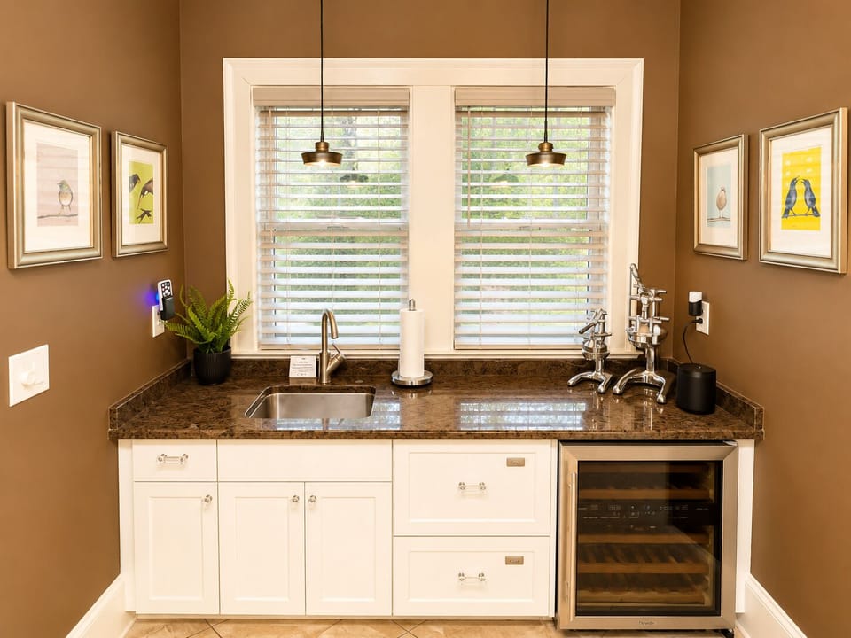 A premium entertaining station featuring custom glass cabinetry, a sink, and a high-end Sub-Zero dual-temperature wine refrigerator. Fully stocked with curated glassware and elite hosting essentials.