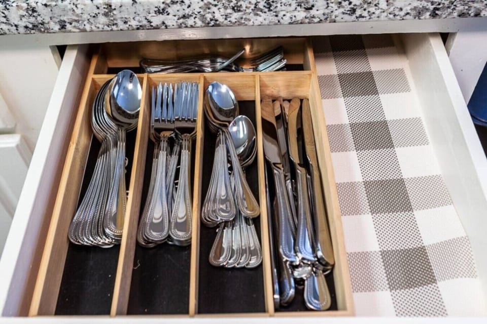 Kitchen cabinet stocked with wine glasses, plates, colorful cups, and utensils.