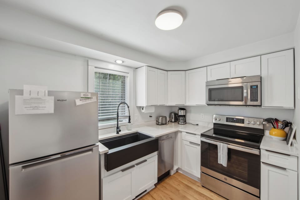 A modern, fully equipped kitchen featuring sleek white cabinetry, a deep farmhouse sink, and stainless steel appliances.