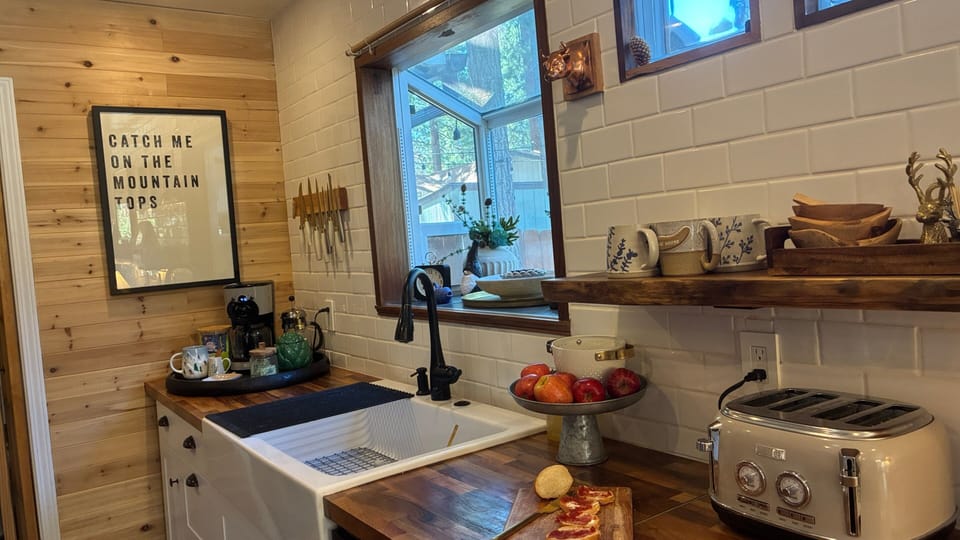 Kitchen counter with sink, small appliances, window, open shelf, and prep space.